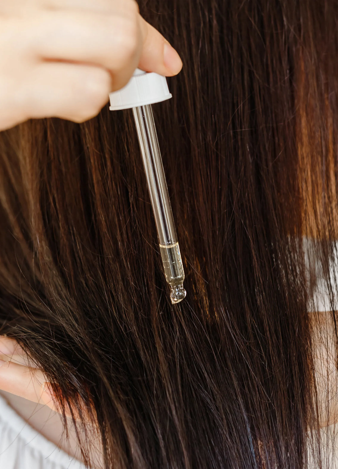 Dropper applying oil treatment to long brown hair